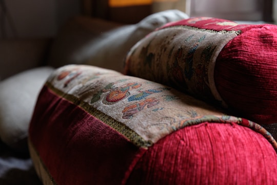 Two intricately patterned cushions with rich red fabric and detailed embroidery rest on a soft surface, creating a cozy and inviting atmosphere in what appears to be a living space with soft lighting.