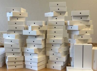 A large number of stacked white boxes, each labeled with the Apple logo and the word 'iPad'. The boxes are neatly arranged in several tall piles on a surface, suggesting a substantial inventory of Apple products.