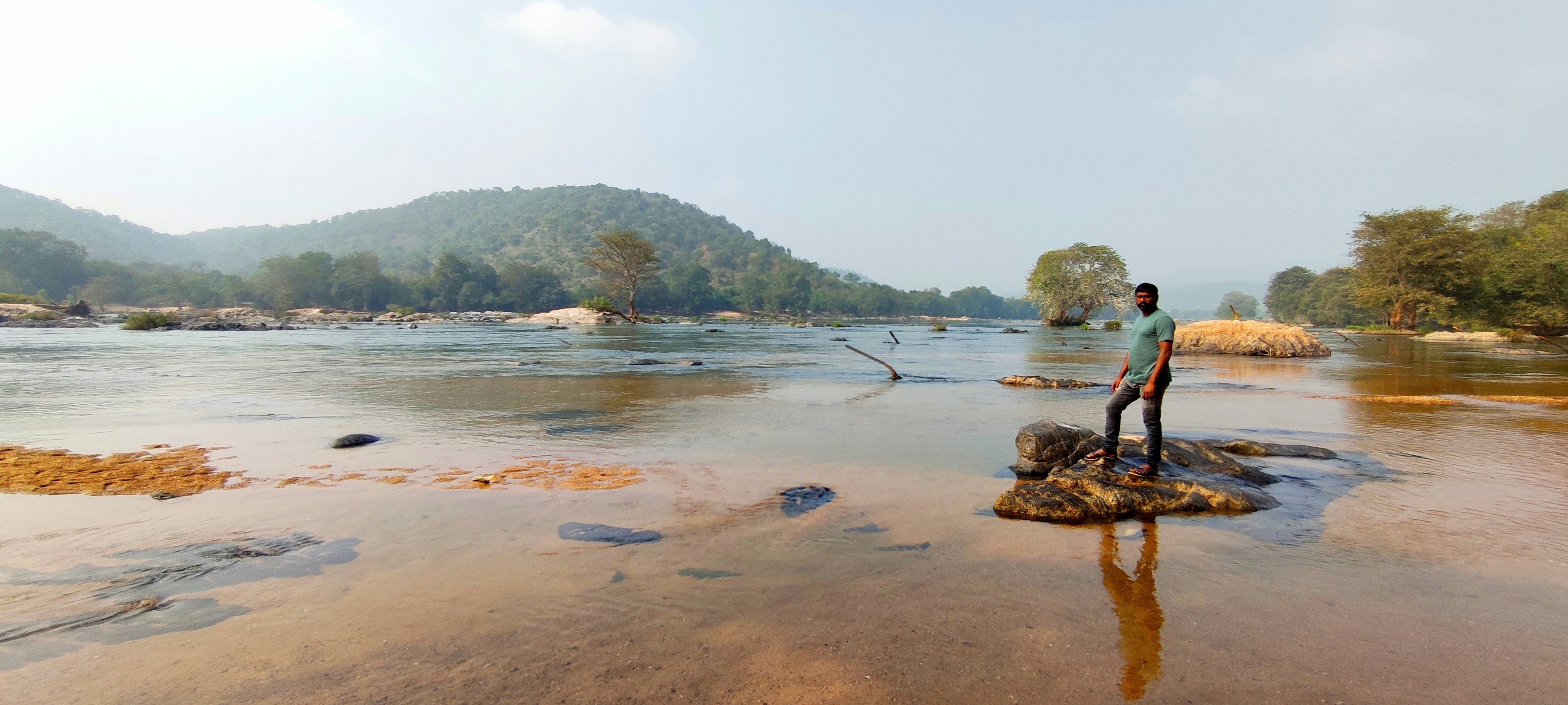 Seorang pria berdiri di atas batu di tengah sungai