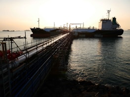 Sunset view of a petroleum tanker docked at a busy port with loading equipment.