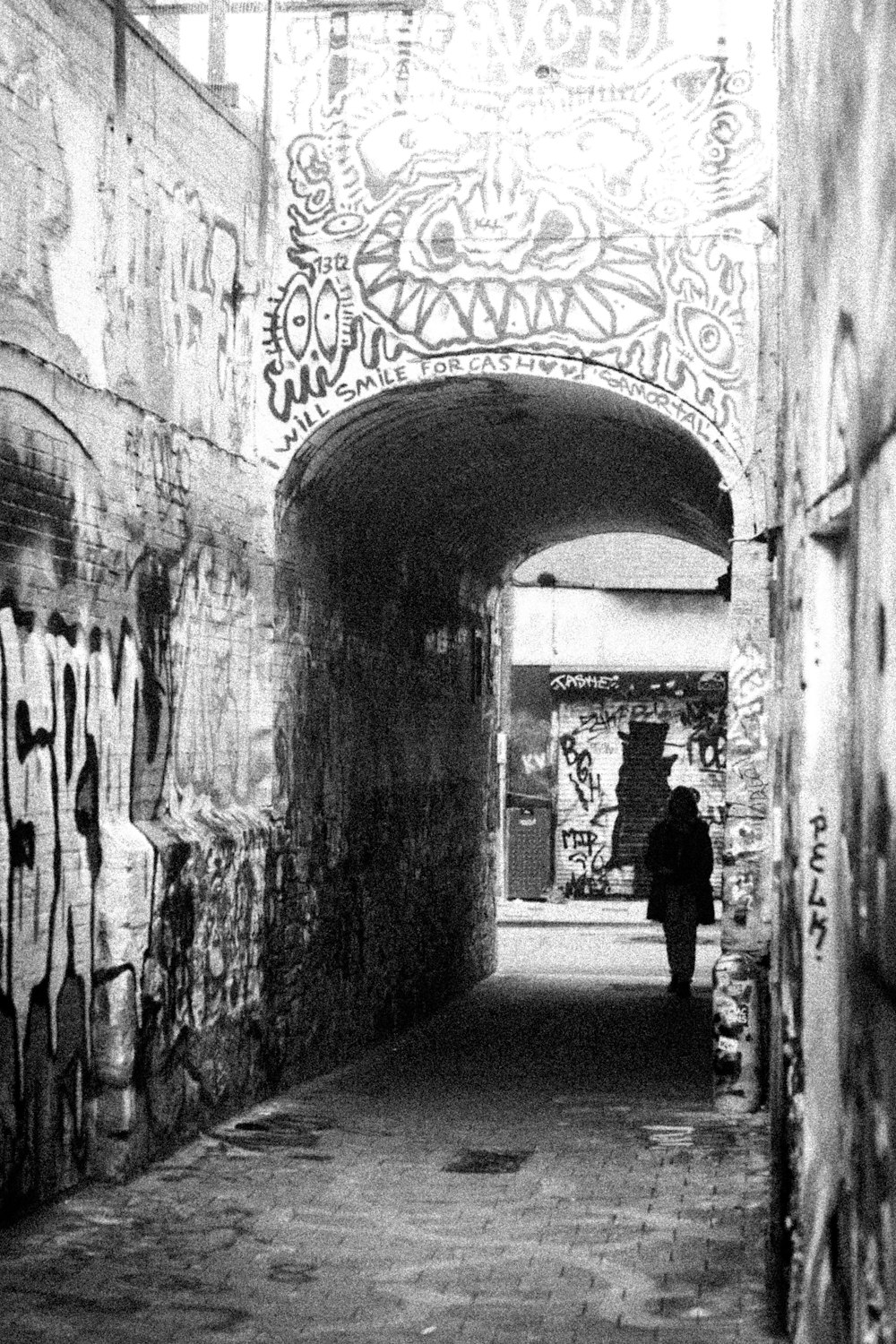 a black and white photo of a person walking through a tunnel