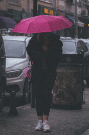 A cheerful person holding a colorful foldable umbrella on a rainy city street.