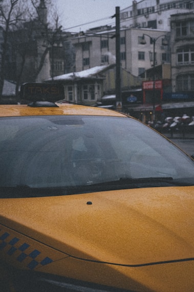 A bright yellow taxi parked beside the snow-capped mountains of Manali under a clear blue sky.