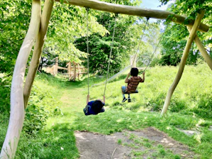 Children playing on swings and climbing frames in a sunny, natural playground area