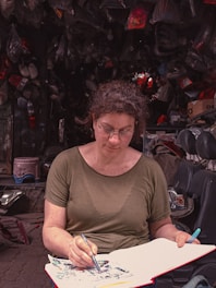 A candid shot of the founder sketching product designs outdoors with camping gear around.