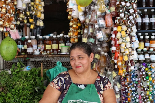 Close-up of a smiling woman holding a bottle of Herbveda herbal capsules in a sunlit herbal garden.