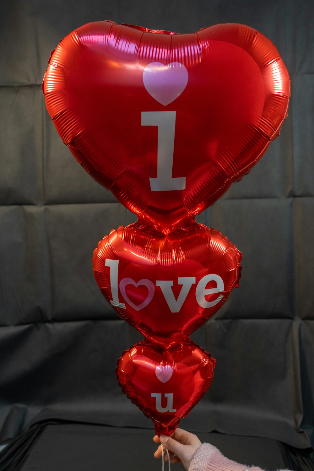 a person holding a bunch of red heart shaped balloons