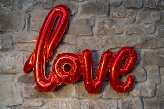 Red foil balloon letters spelling the word 'love' are mounted against a rustic stone wall.
