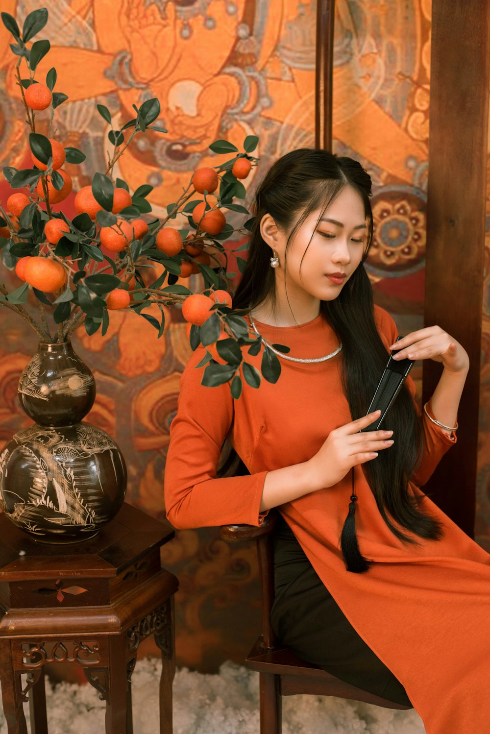 a woman sitting on a chair next to a vase of oranges