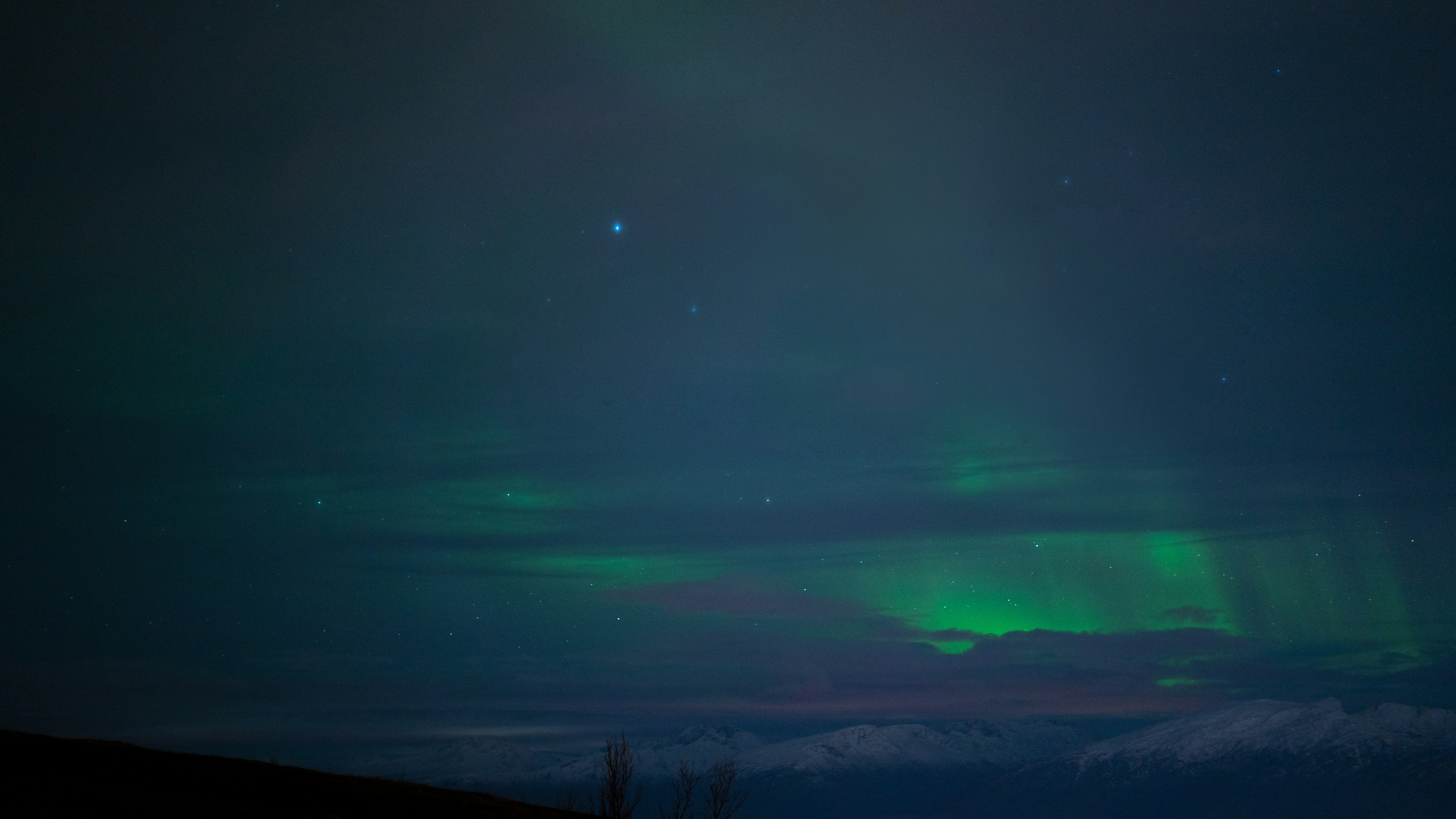 Nordlys i grønt og hvitt over snødekte fjell i Nord-Norge om natten
