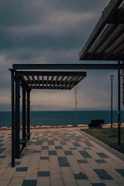a bench sitting under a covered walkway next to the ocean
