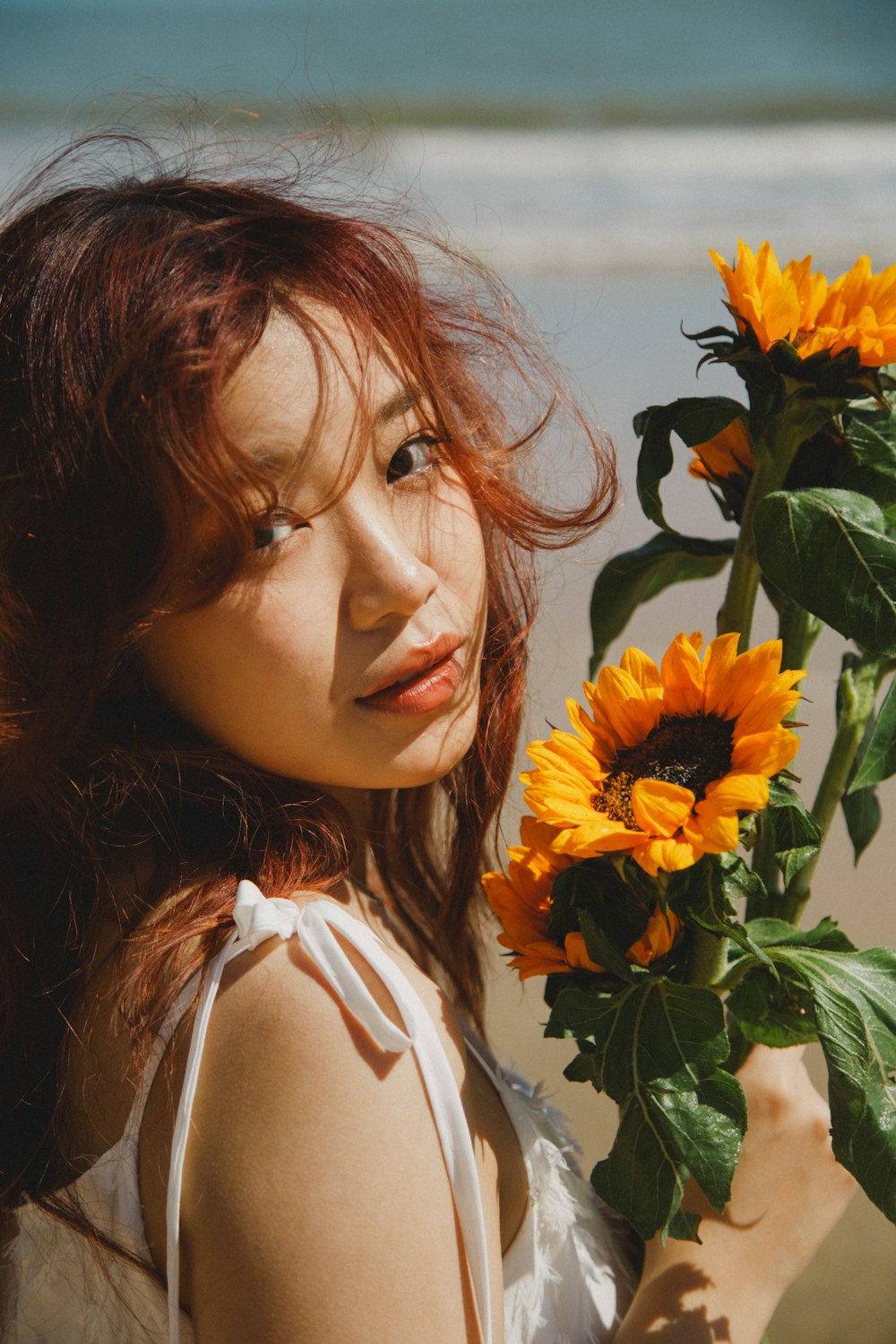 a woman holding a sunflower in front of a body of water