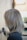 A person with light brown hair, featuring shades of ash and silver, styled in a smooth and slightly layered cut seen from the side. The background is softly blurred, suggesting an indoor environment possibly in a salon.