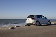 A modern silver sedan parked beside a small pier jutting out into calm turquoise water.