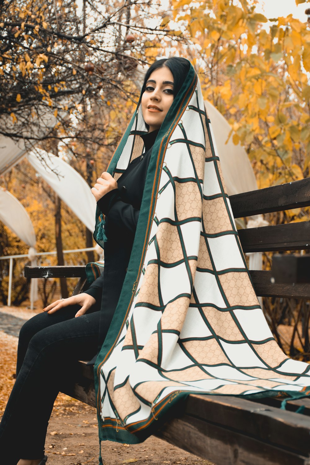 a woman sitting on a park bench under a blanket