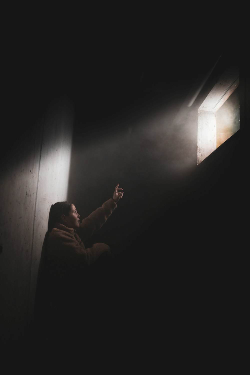 a man in a dark room pointing at the light coming through the window