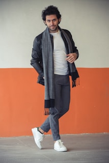 Casual chic: a man in a soft gray sweater and dark jeans leaning against a textured brick wall.