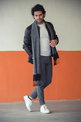 A man dressed in a sharp khawani & co blazer paired with casual jeans, leaning against a rustic brick wall.