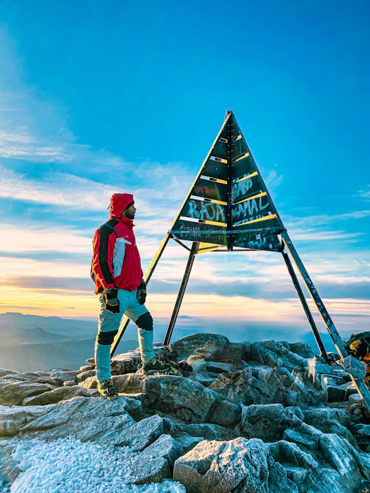 A hiker wearing vibrant outdoor clothing standing on a rocky mountain peak at sunrise.