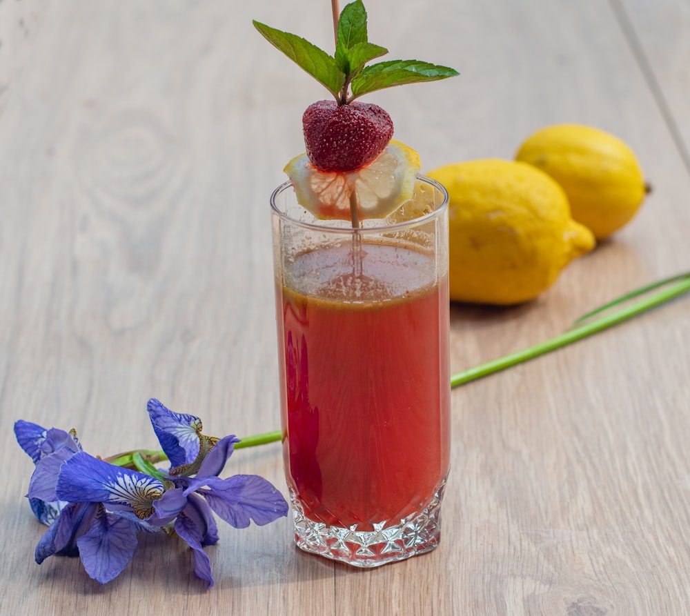 a glass filled with liquid next to lemons and a flower