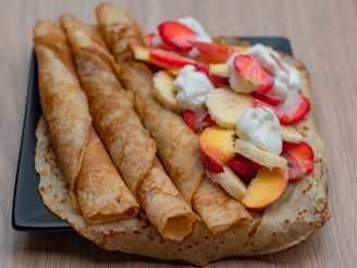 a black plate topped with crepes covered in fruit