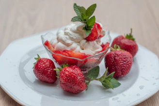 Close-up of fresh strawberries topped with whipped cream in a delicate glass bowl.