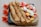 Three rolled crepes are placed on a square black plate with an additional unfolded crepe beside them. The unfolded crepe is topped with slices of strawberries, bananas, and peaches, along with dollops of whipped cream. Bright orange flowers artfully decorate the backdrop on the wooden table surface.