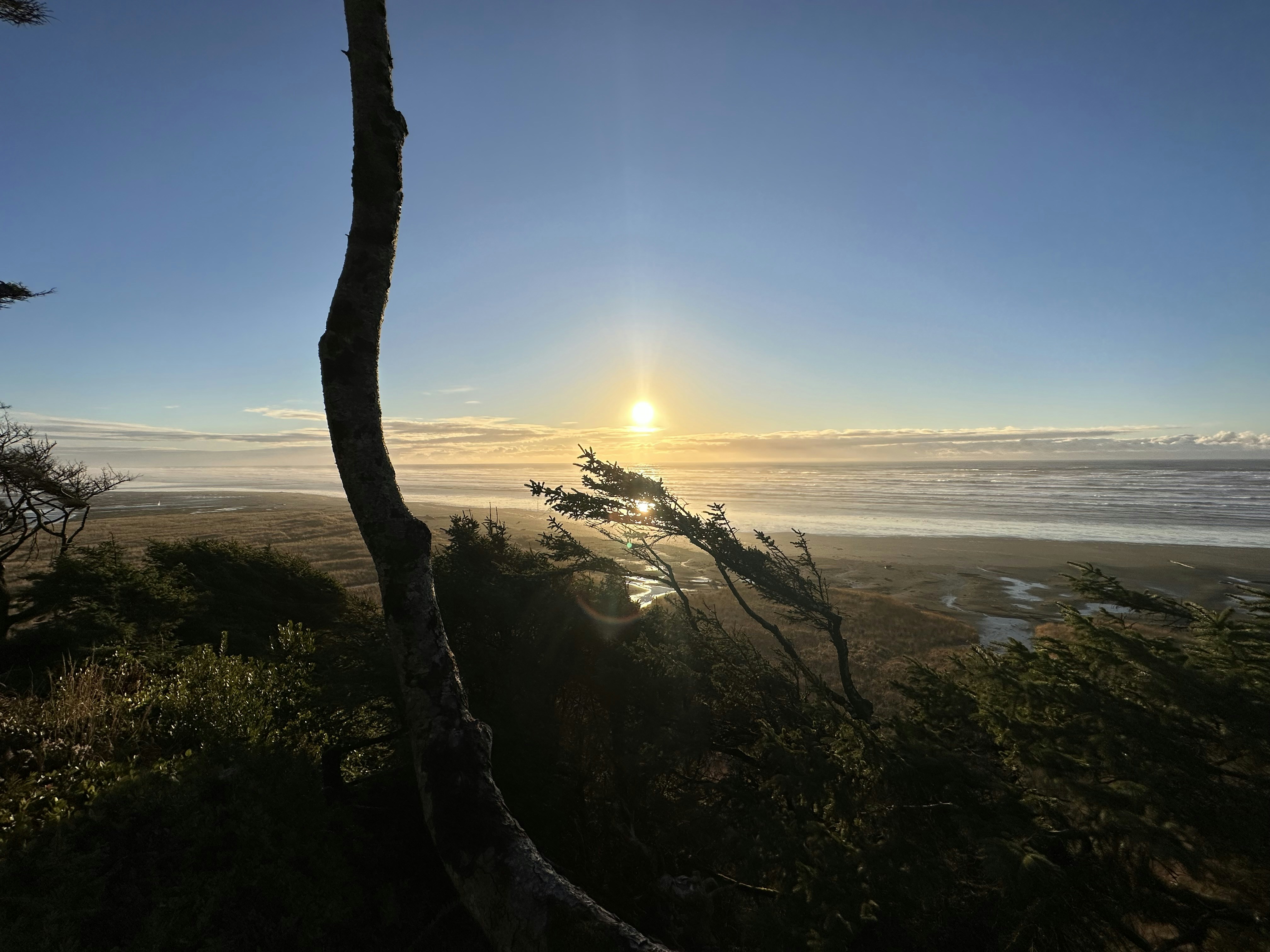 the sun is setting over the ocean from a hill