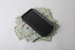 Close-up of hands exchanging money with a digital phone in the background showing earnings.