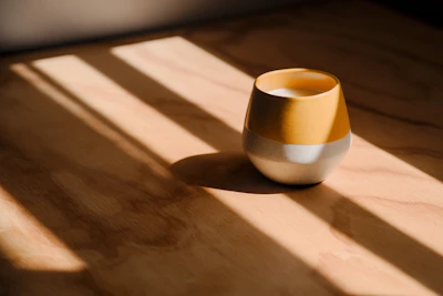 A bright, hand-thrown stoneware bowl in cheerful yellow resting on a wooden table with soft natural light.