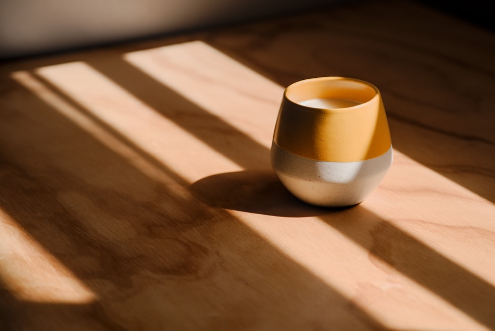 a yellow and white vase sitting on top of a wooden table