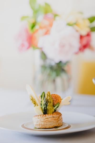 a plate of food on a table with a vase of flowers in the background