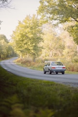 A group of classic American cars cruising through a scenic Loire Valley countryside road.