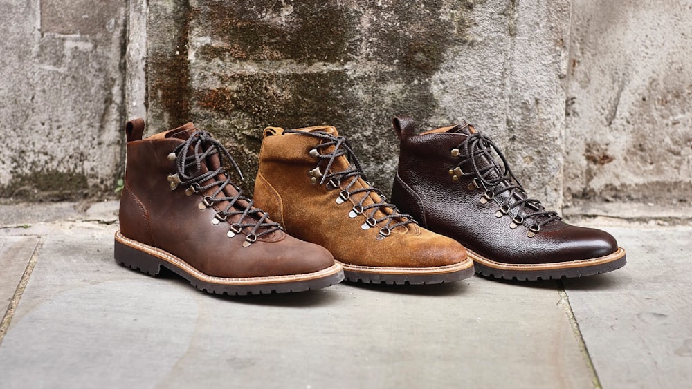 three pairs of boots are lined up against a stone wall