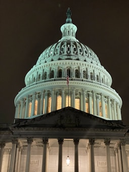 Detailed architectural facade of a domed government building illuminated at night, adorned with columns and intricate sculptures.