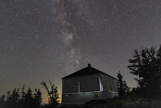 A clear night sky with Starlink satellites orbiting above a remote mountain cabin.