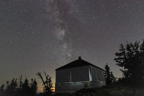A clear night sky with Starlink satellites orbiting above a remote mountain cabin.