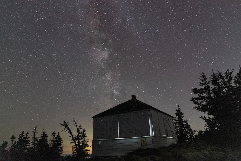a small house sitting on top of a hill under a night sky filled with stars