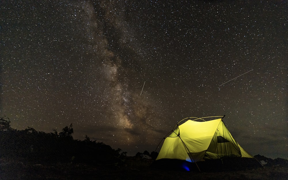 a tent pitched up against a night sky with the milky in the background