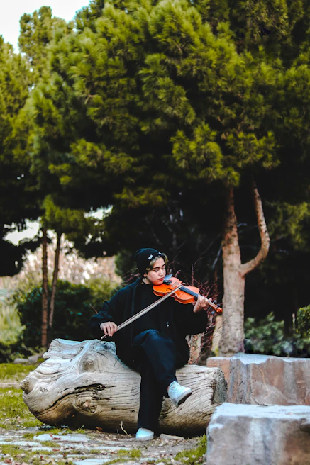 Seadi in a sunlit park holding a violin, surrounded by nature, reflecting his connection to environmental themes.