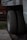 Two truck tires are positioned side by side beneath a vehicle chassis, resting on a concrete surface. The background includes a wooden structure and a red object, possibly a tool or equipment, on a platform. The setting seems to be an outdoor or garage area with patches of grass visible.