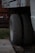 Two truck tires are positioned side by side beneath a vehicle chassis, resting on a concrete surface. The background includes a wooden structure and a red object, possibly a tool or equipment, on a platform. The setting seems to be an outdoor or garage area with patches of grass visible.