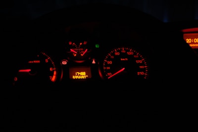 A dimly lit car dashboard displays several illuminated gauges, including a speedometer and tachometer, primarily showing in red light. The odometer reads 17488, with a trip meter showing 33560.1 km. A digital clock on the right side shows the time as 20:05.