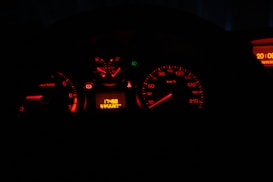 A dimly lit car dashboard displays several illuminated gauges, including a speedometer and tachometer, primarily showing in red light. The odometer reads 17488, with a trip meter showing 33560.1 km. A digital clock on the right side shows the time as 20:05.