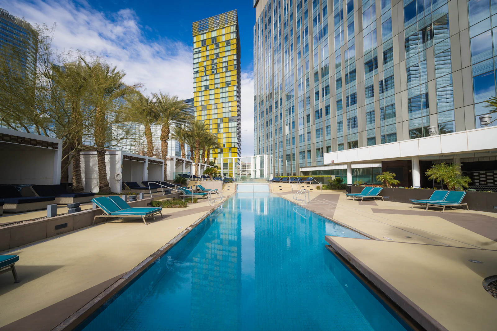 A resort pool deck lined with lounge chairs beneath Strip hotel towers.