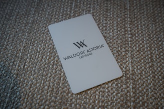 A white card with the Waldorf Astoria Las Vegas logo is placed on a textured, woven surface.
