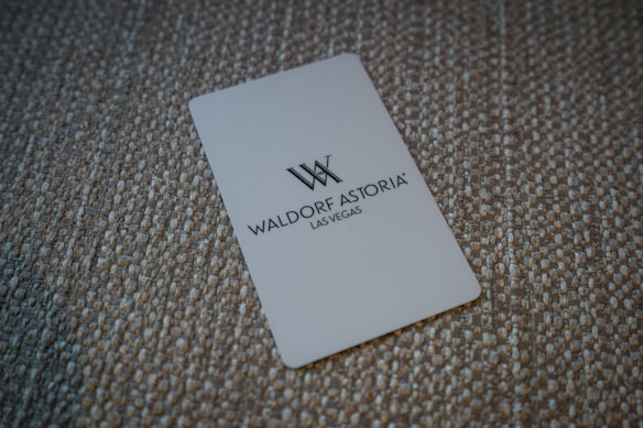 A white card with the Waldorf Astoria Las Vegas logo is placed on a textured, woven surface.