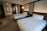 A modern hotel room with two neatly made queen-size beds featuring white sheets and pillows. The walls have an elegant design with patterned panels accompanied by soft ambient lighting. There's a subtle division between the sleeping area and a glass-enclosed shower area.