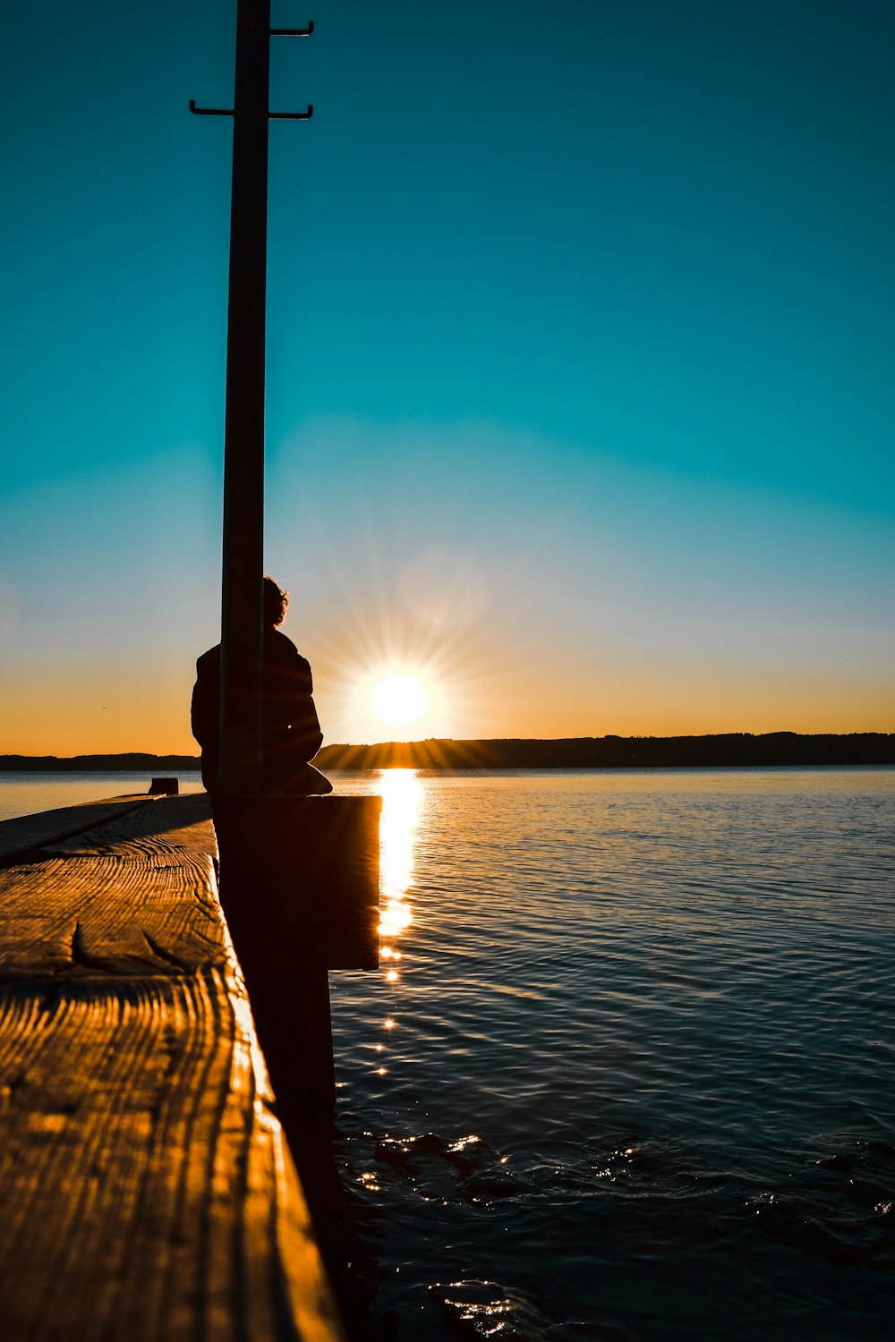 Una persona seduta su un molo che guarda il sole tramontare