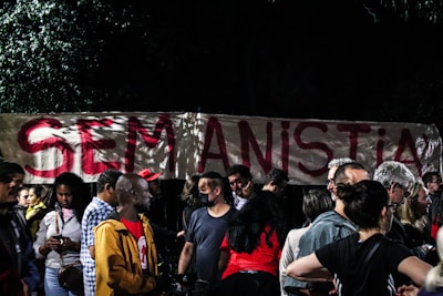 A group of people gathered in front of a large banner with the phrase 'SEM ANISTIA' written in bold red letters. The setting appears to be nighttime, with trees partially visible in the background.